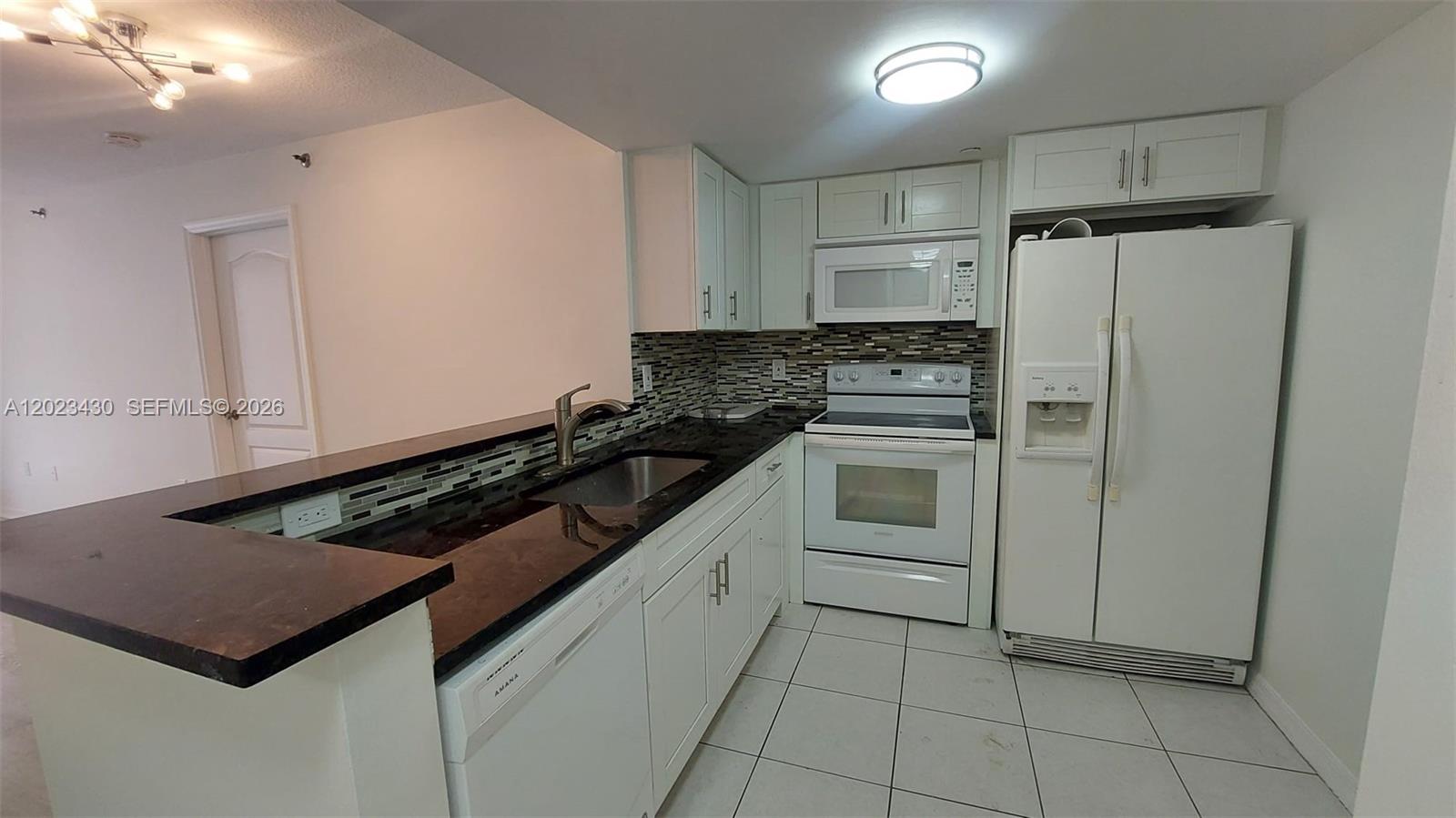 A kitchen features white cabinets, dark countertops, white appliances, and a tiled backsplash — 2642 Collins Ave # 408, Miami Beach FL 33140, MIAMI BEACH, FL