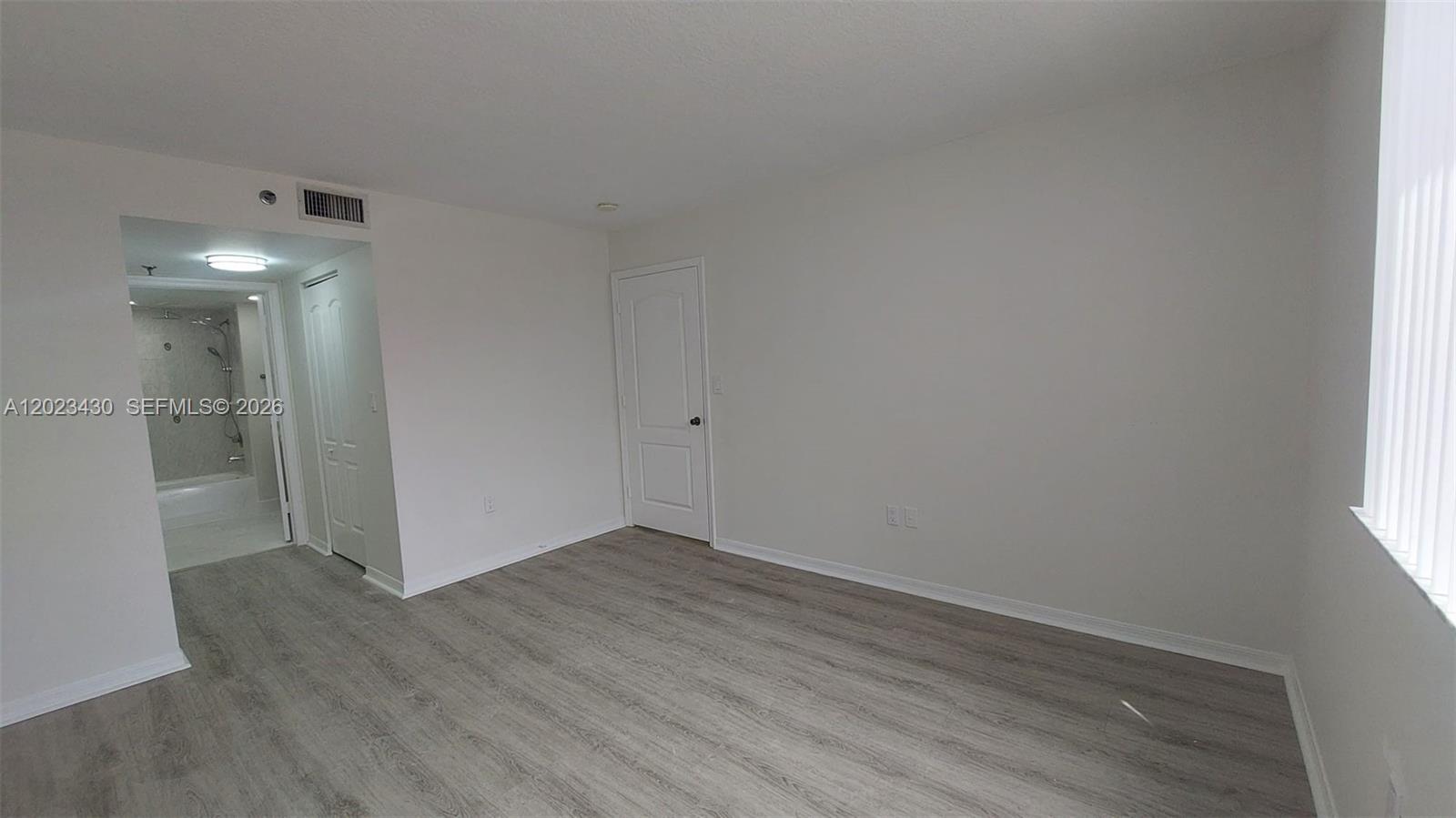 An empty room features light-colored wood-look flooring, white walls, and an attached bathroom — 2642 Collins Ave # 408, Miami Beach FL 33140, MIAMI BEACH, FL