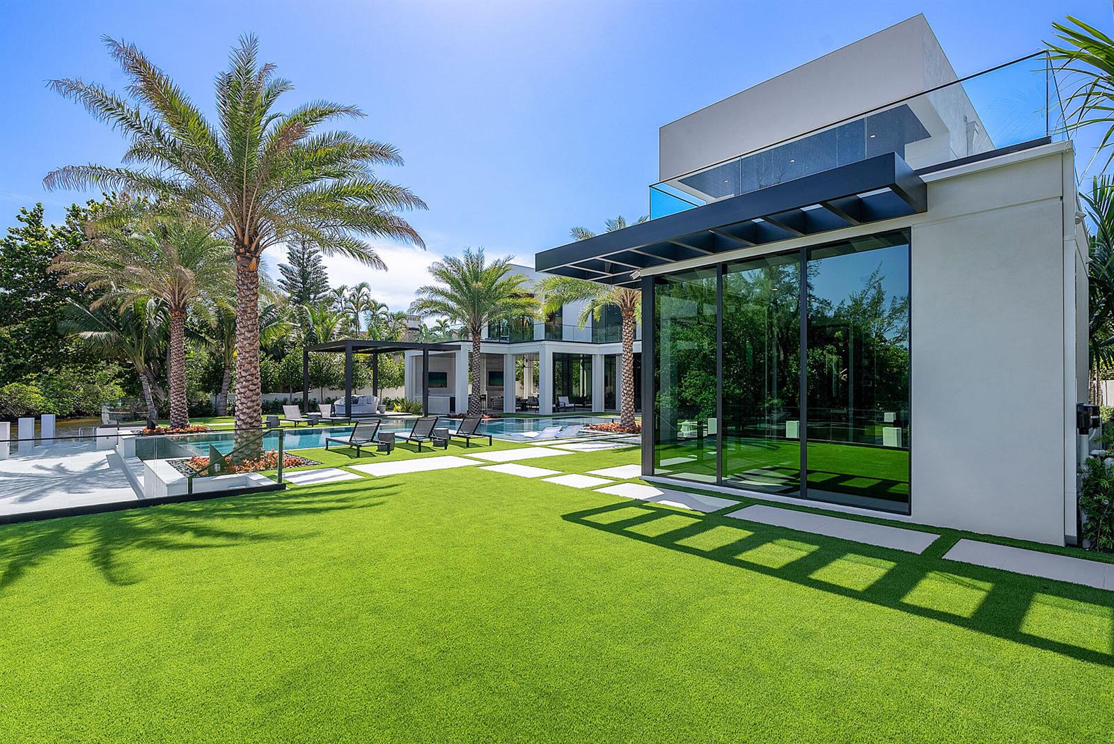 A modern house with large glass walls, a swimming pool, and palm trees on a lawn — 372 E Alexander Palm Road, Boca Raton FL 33432, BOCA RATON, FL