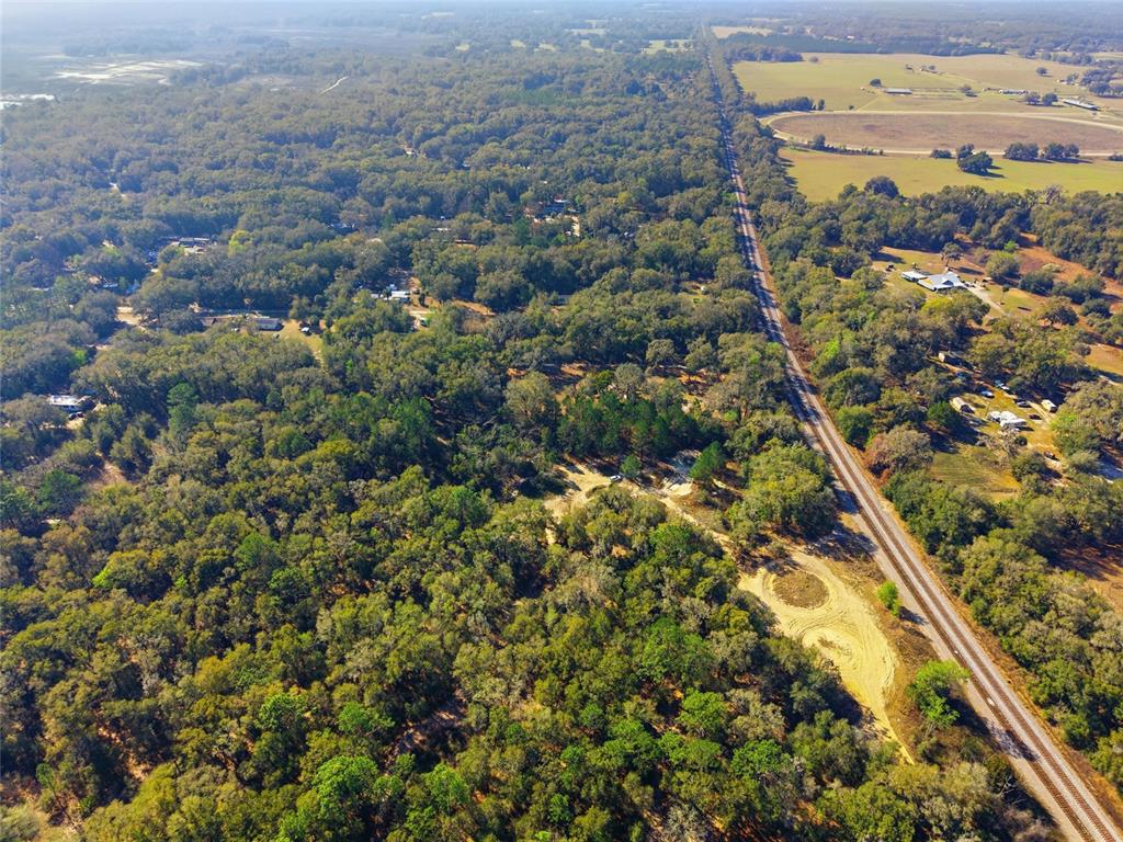 An aerial view shows a wooded area adjacent to a railroad track and open fields — Lot 027 NE 164TH LANE, CITRA, FL