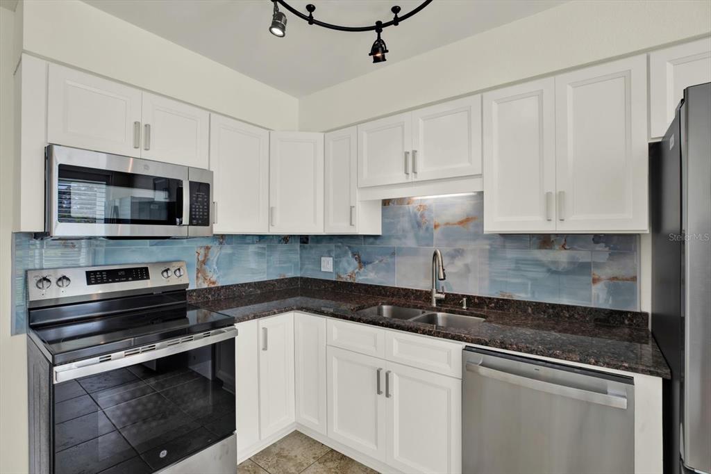 A kitchen features white cabinets, dark granite countertops, stainless steel appliances, and blue tile backsplash — 4715 BAY STREET NE UNIT 126, ST PETERSBURG, FL