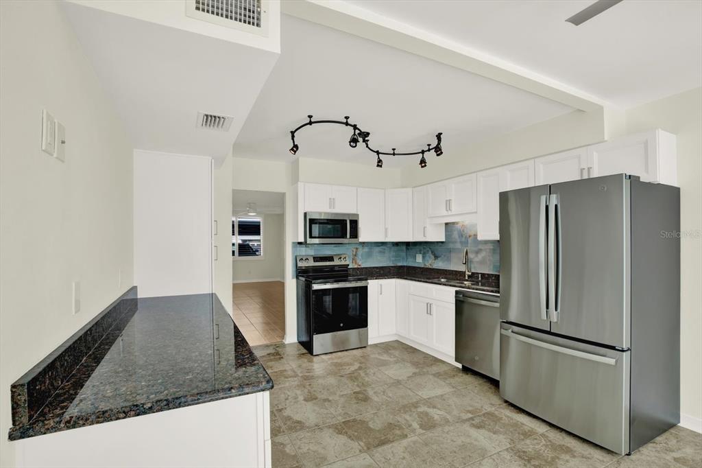 A kitchen features white cabinets, dark granite countertops, stainless steel appliances, and tile flooring — 4715 BAY STREET NE UNIT 126, ST PETERSBURG, FL