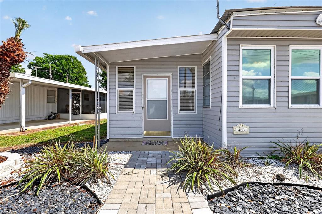The exterior of a gray mobile home features a covered entryway and a paved walkway — 465 MARINA LANE, TAVARES, FL