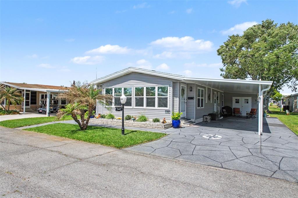 A gray manufactured home features a paved driveway, a carport, and a small front lawn — 319 MELBOURN DRIVE, HAINES CITY, FL