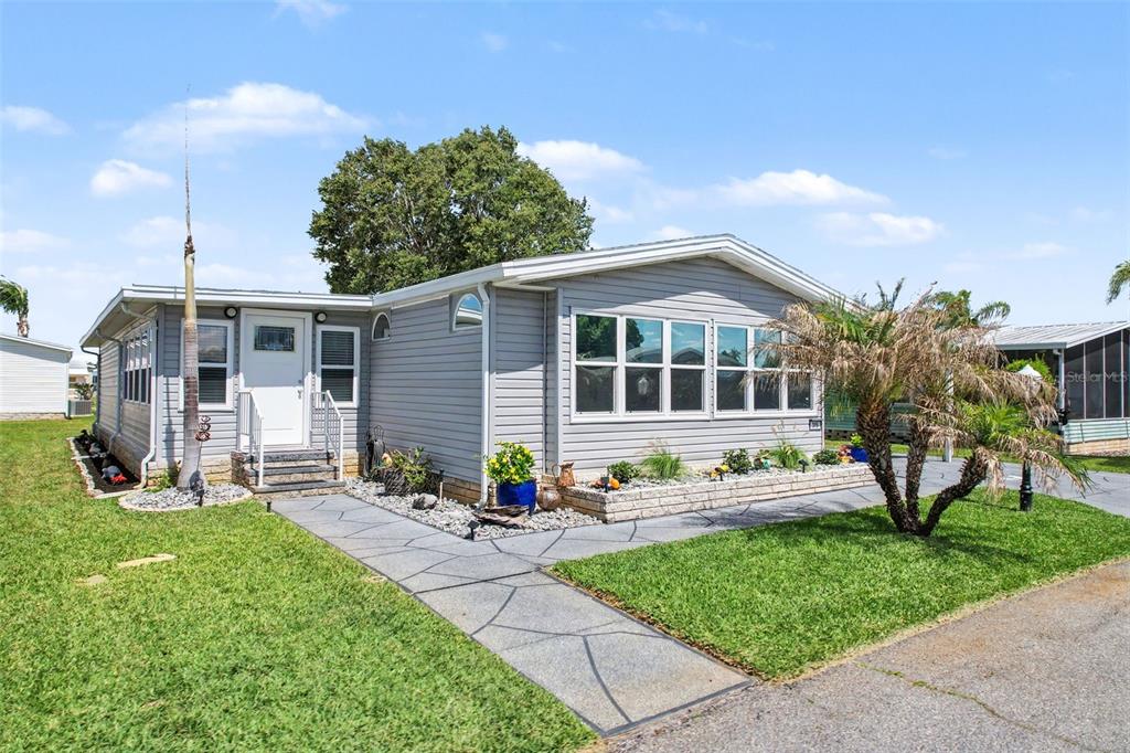 A gray manufactured home features a stone walkway, a small palm tree, and landscaping — 319 MELBOURN DRIVE, HAINES CITY, FL