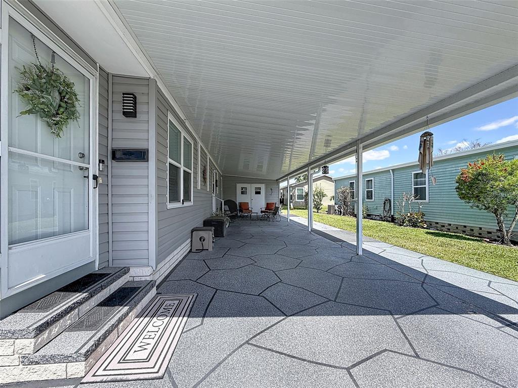 A covered concrete patio with a patterned finish runs alongside a gray mobile home — 319 MELBOURN DRIVE, HAINES CITY, FL