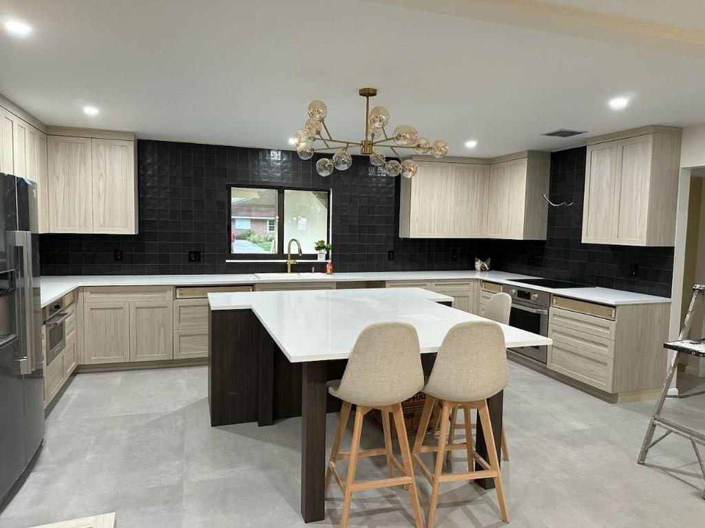A modern kitchen features light wood cabinets, a dark tile backsplash, and a white island — 7676 Overlook Drive, Lake Worth FL 33467, LAKE WORTH, FL