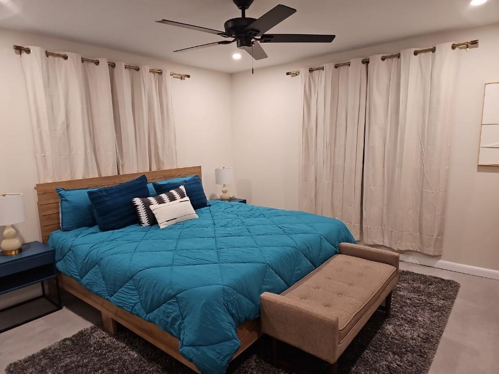 A bedroom features a wooden bed frame, teal bedding, a bench, and two windows with curtains — 7676 Overlook Drive, Lake Worth FL 33467, LAKE WORTH, FL