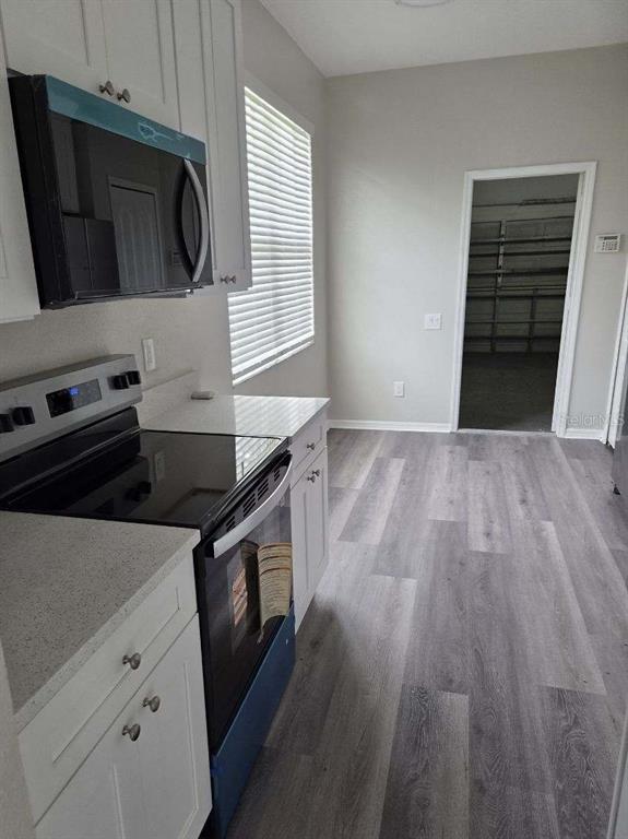 A kitchen features white cabinets, a black stove and microwave, and gray wood-look flooring — 9321 HUNTINGTON PARKWAY, TAMPA, FL