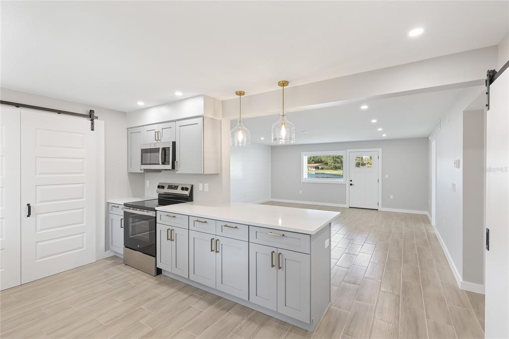 A kitchen with light gray cabinets and white countertops opens into a bright living area — 4444 NARRAGANSET TRAIL UNIT 96, SARASOTA, FL