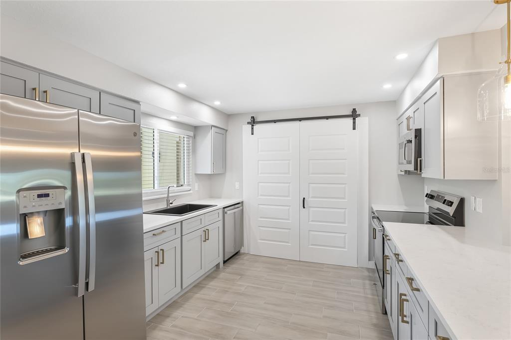 A modern kitchen features gray cabinets, stainless steel appliances, white countertops, and white barn doors — 4444 NARRAGANSET TRAIL UNIT 96, SARASOTA, FL