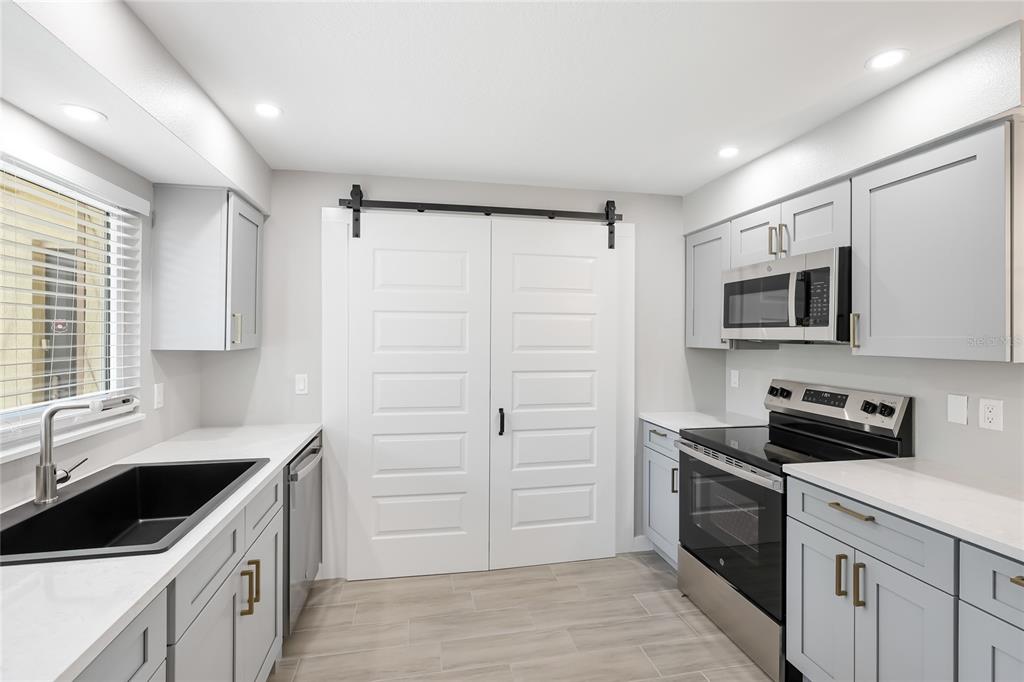A modern kitchen features light gray cabinets, white countertops, a black sink, and white barn doors — 4444 NARRAGANSET TRAIL UNIT 96, SARASOTA, FL