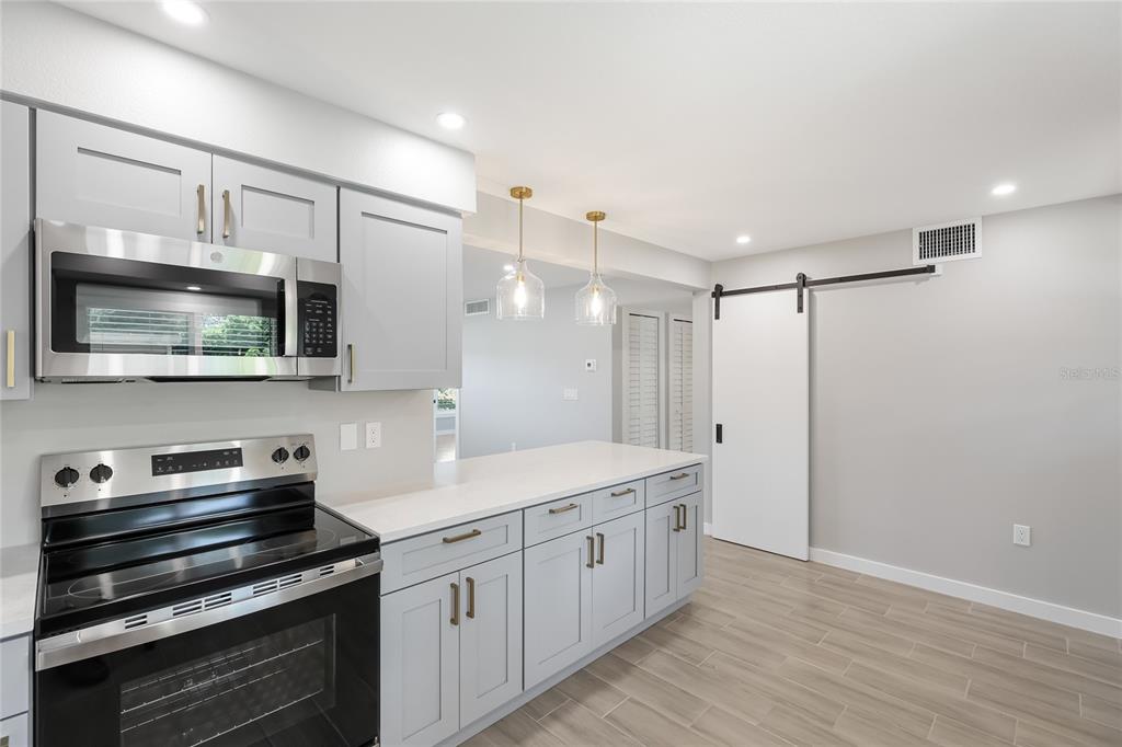 A modern kitchen features light gray cabinets, stainless steel appliances, and a white barn door — 4444 NARRAGANSET TRAIL UNIT 96, SARASOTA, FL