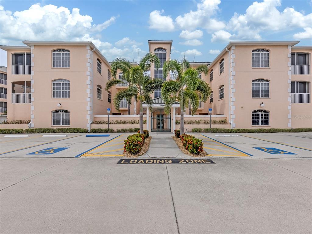 A three-story peach-colored apartment building features a central entrance, palm trees, and parking spaces — 1505 GONDOLA PARK DRIVE UNIT 1505, VENICE, FL