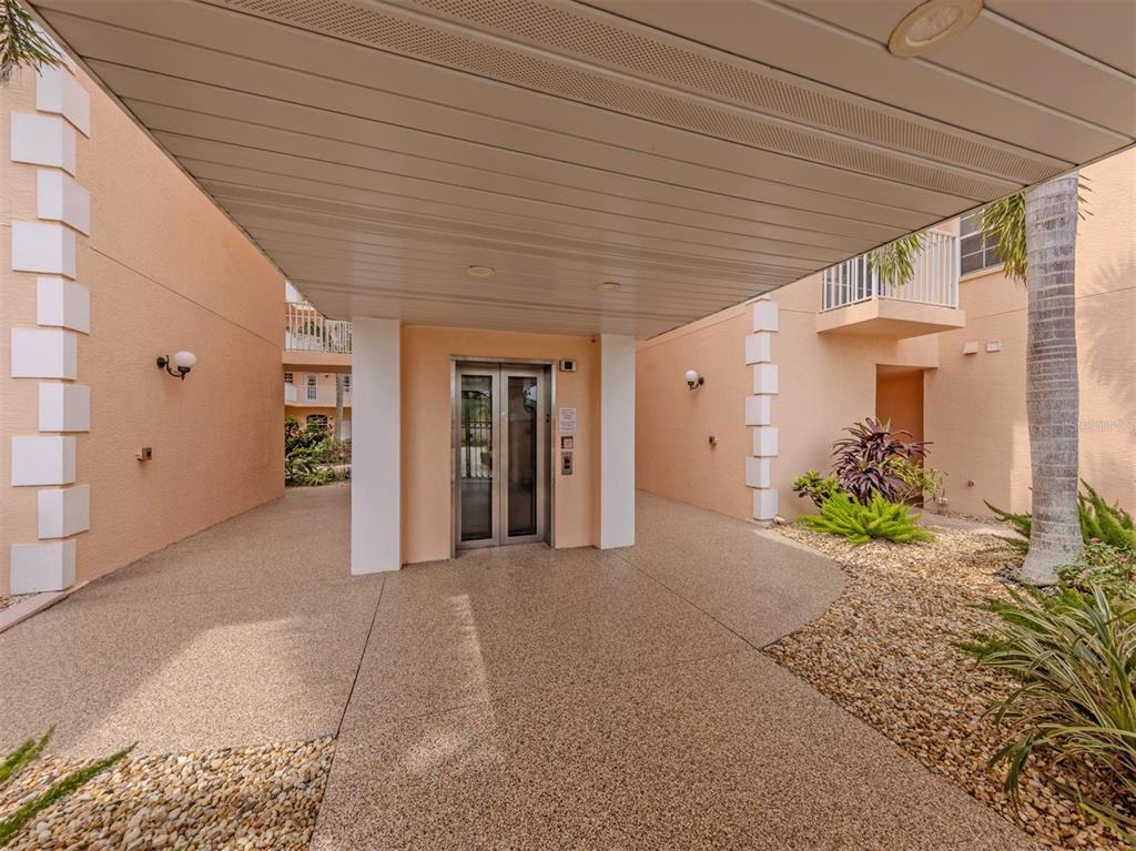 An outdoor elevator entrance is covered by a white carport with a pebble-textured driveway — 1505 GONDOLA PARK DRIVE UNIT 1505, VENICE, FL