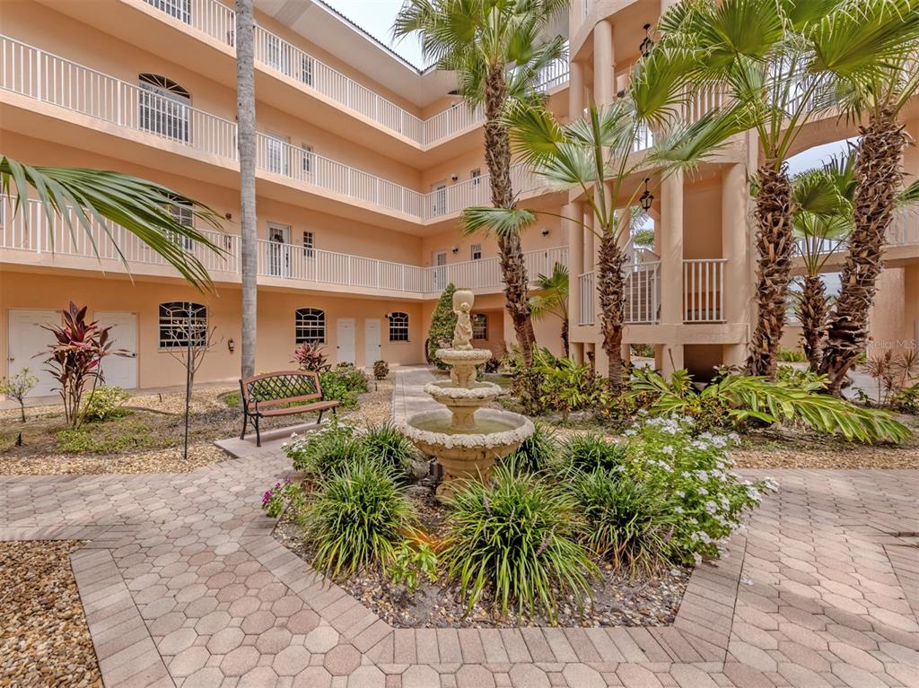 An outdoor courtyard features a stone fountain, palm trees, and a multi-story peach-colored building — 1505 GONDOLA PARK DRIVE UNIT 1505, VENICE, FL