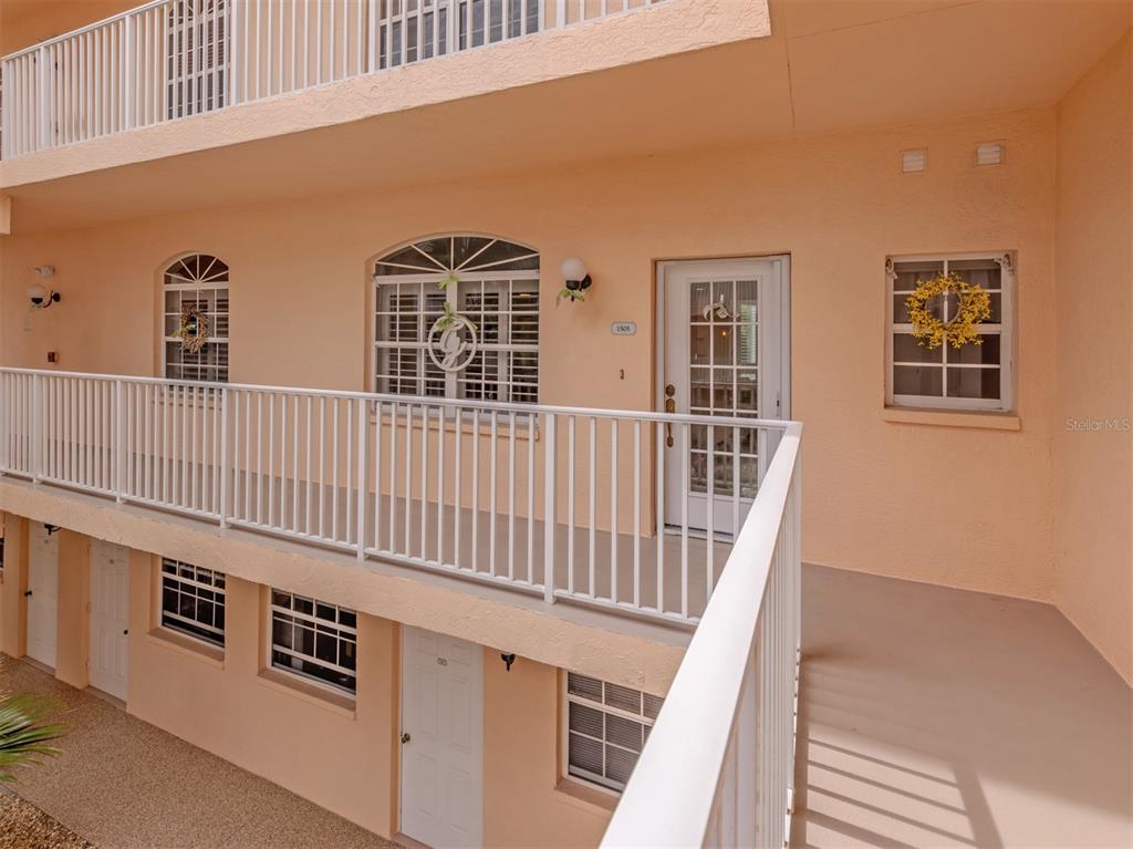 An exterior view of a two-story apartment building with peach-colored stucco walls and white railings — 1505 GONDOLA PARK DRIVE UNIT 1505, VENICE, FL