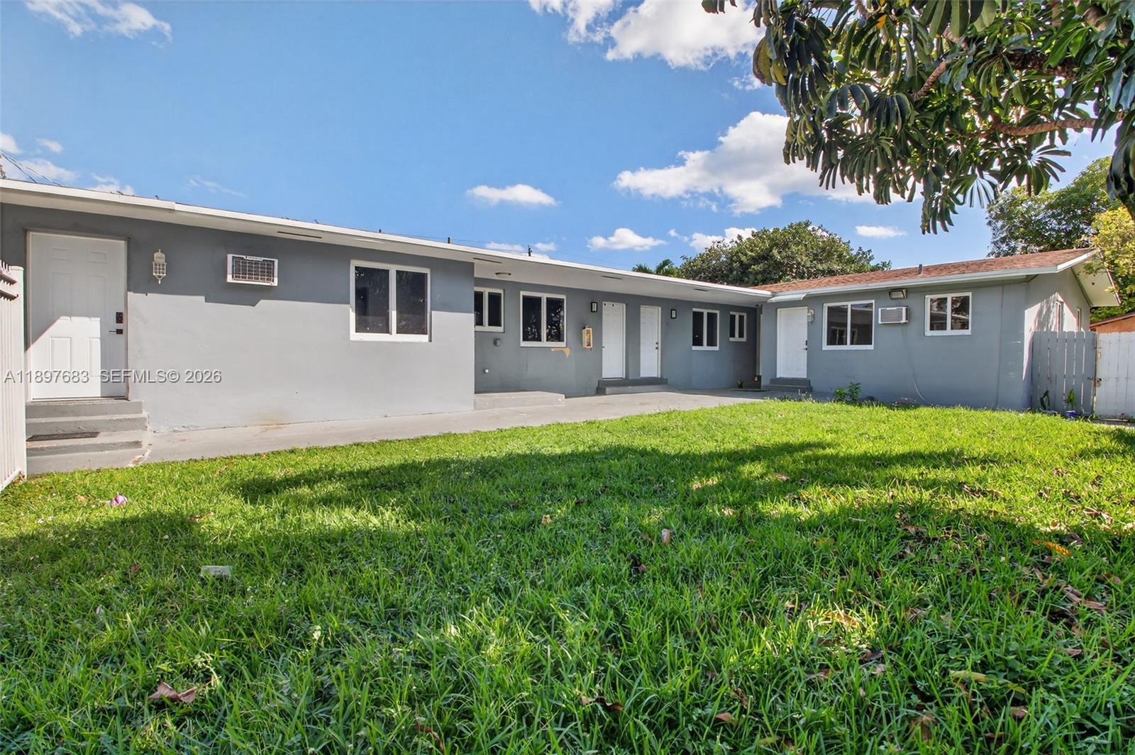 An exterior view of a single-story gray building with multiple doors and a grassy yard — 1864 NW 28th St, Miami FL 33142, MIAMI, FL