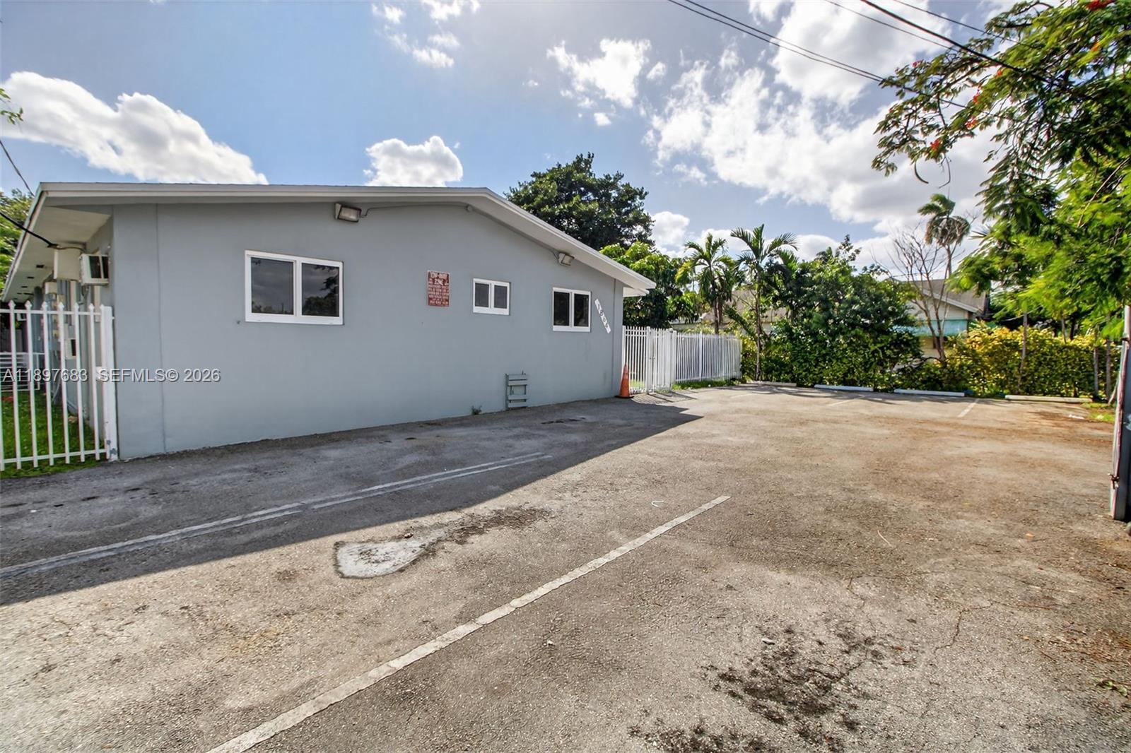 The exterior of a gray building features a parking lot and a white metal fence — 1864 NW 28th St, Miami FL 33142, MIAMI, FL