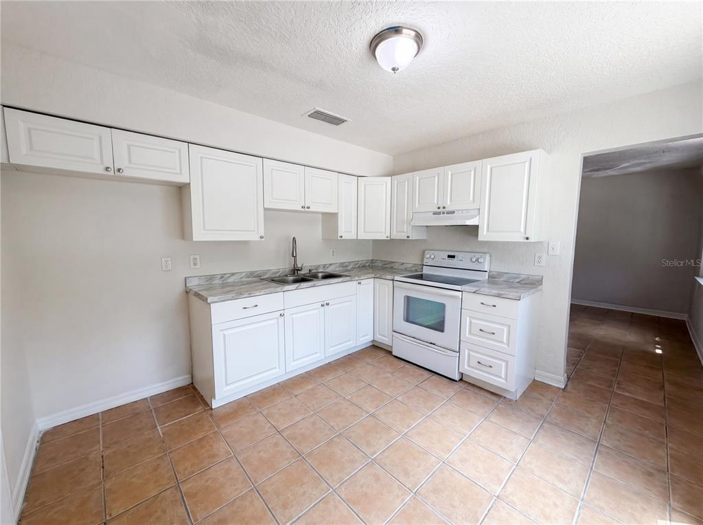 A kitchen features white cabinets, a white stove, a sink, and tan tile flooring — 4010 E PARIS STREET, TAMPA, FL