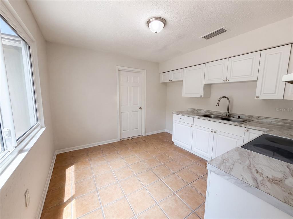 A kitchen features white cabinets, marble-look countertops, and light-colored tile flooring — 4010 E PARIS STREET, TAMPA, FL