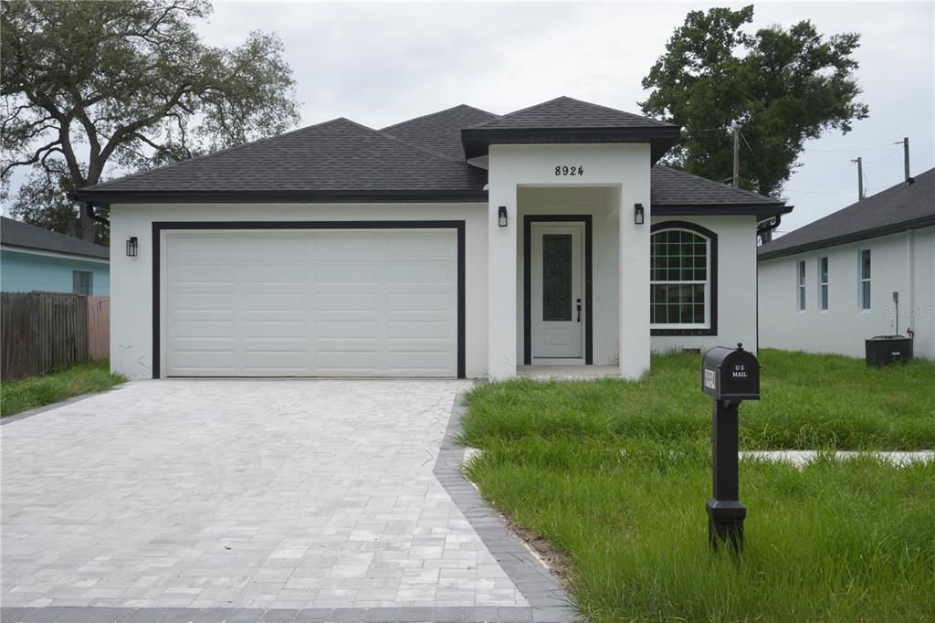 A single-story house with a white stucco facade, black trim, and a paved driveway — 8924 N ORLEANS AVENUE, TAMPA, FL