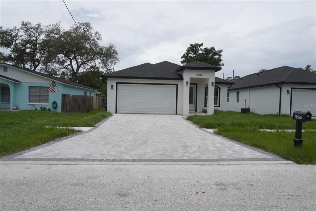 A single-story house with a white exterior, a paved driveway, and a dark shingled roof — 8924 N ORLEANS AVENUE, TAMPA, FL