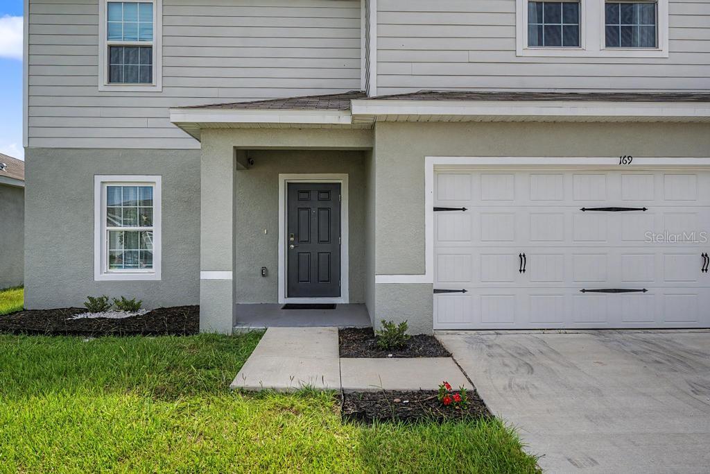 A two-story house exterior features a gray front door, a white garage, and light-colored siding — 169 BORLAND STREET, BROOKSVILLE, FL