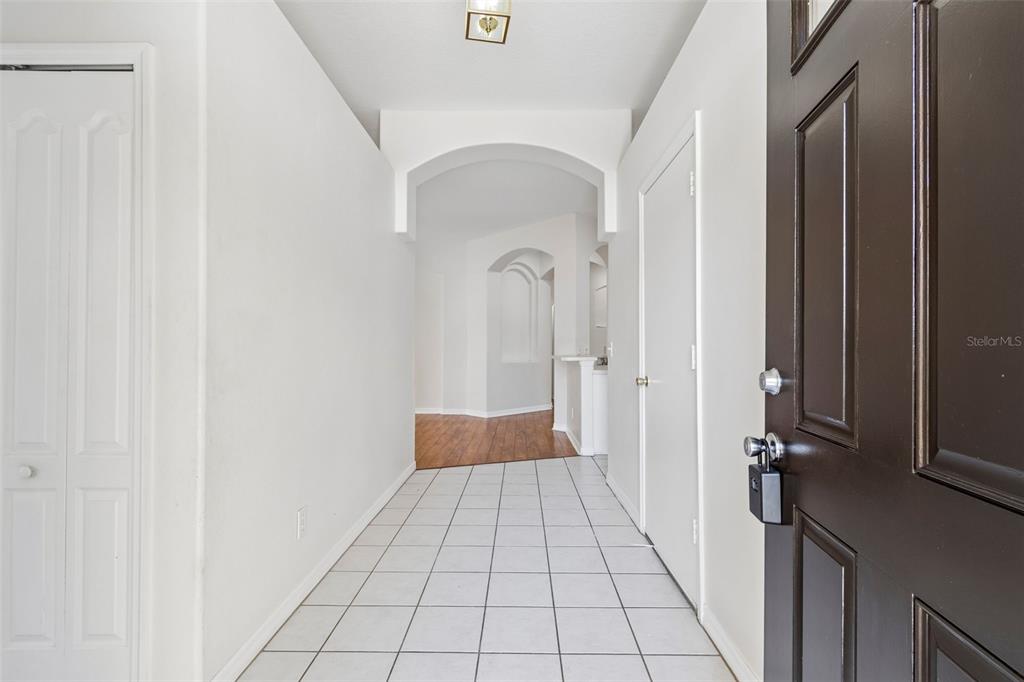 A tiled entryway leads to a hallway with arched openings and wood-look flooring — 1229 CRIMSON CLOVER LANE, WESLEY CHAPEL, FL