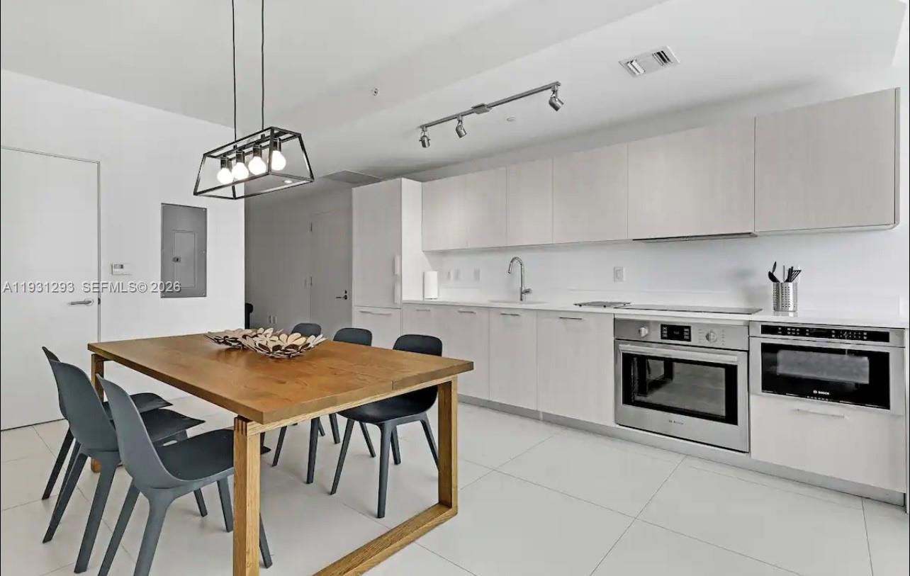 A modern kitchen features white cabinetry, stainless steel appliances, and a wooden dining table — 501 NE 31st St # 1607, Miami FL 33137, MIAMI, FL