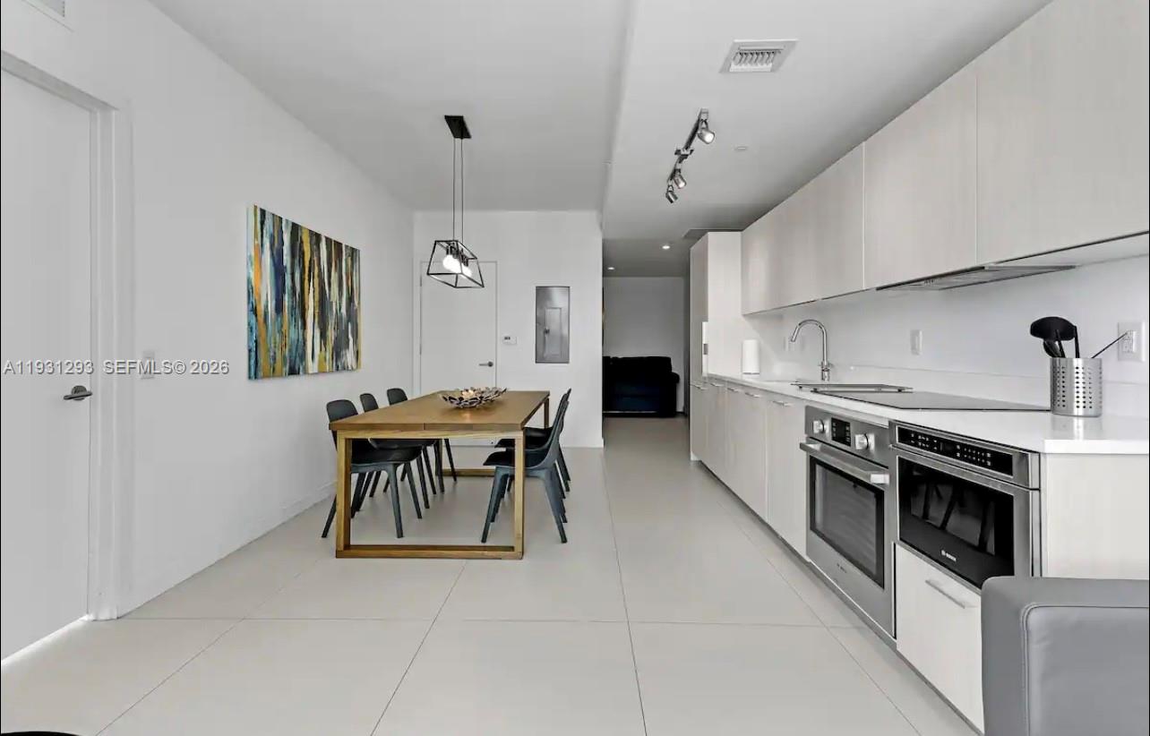 A modern kitchen and dining area with white cabinets, stainless steel appliances, and tile flooring — 501 NE 31st St # 1607, Miami FL 33137, MIAMI, FL
