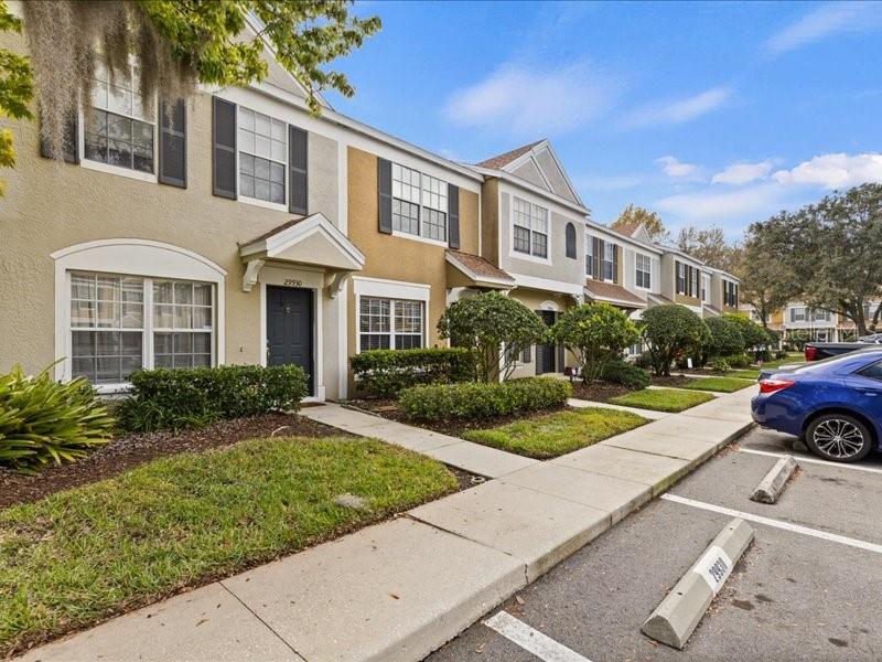 A row of multi-story townhomes features tan and beige stucco facades with dark window shutters — 29924 PLAYA DEL REY LANE, WESLEY CHAPEL, FL