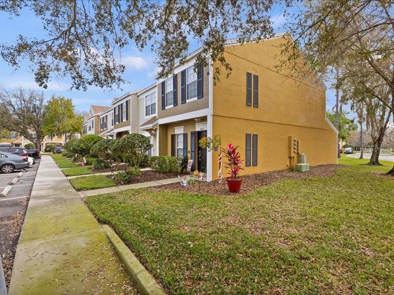 A multi-story yellow townhouse with dark shutters sits next to a sidewalk and parking lot — 29924 PLAYA DEL REY LANE, WESLEY CHAPEL, FL