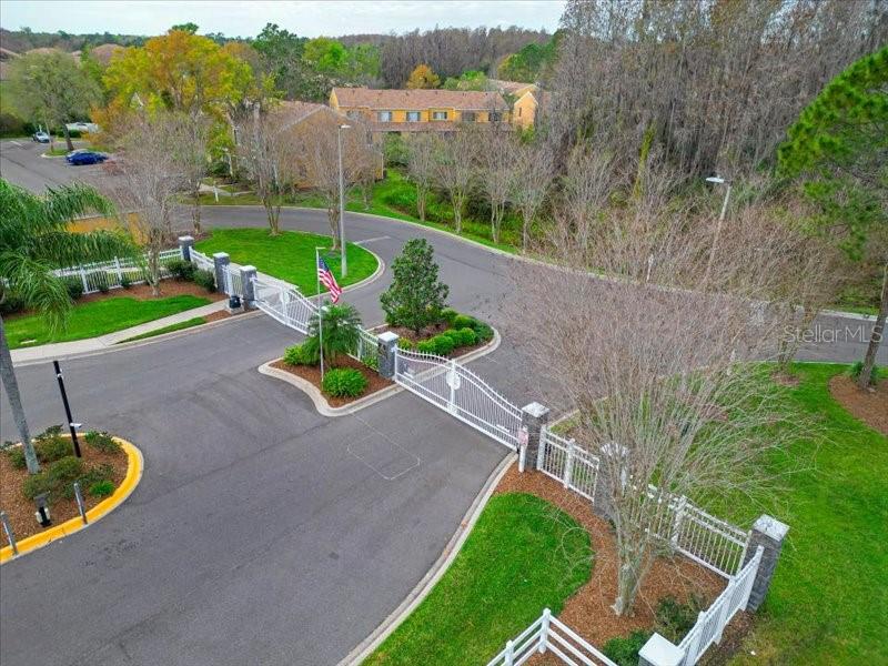 An aerial view shows a gated community entrance with a white fence and an American flag — 29924 PLAYA DEL REY LANE, WESLEY CHAPEL, FL