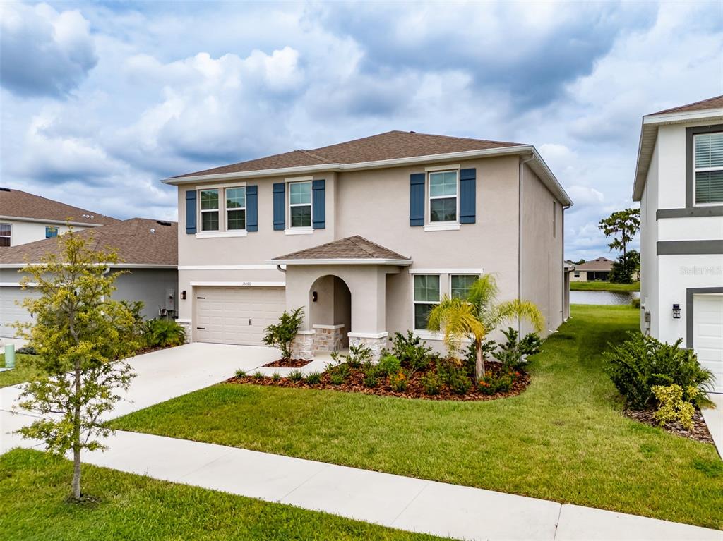 A two-story suburban house with a beige stucco exterior, blue shutters, and a front garage — 13090 BROOKSIDE MOSS DRIVE, RIVERVIEW, FL