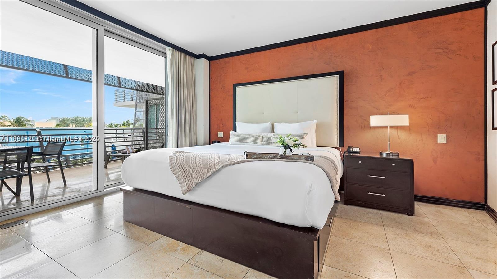 A bedroom features a bed with a large headboard, tile flooring, and a balcony view — 1437 Collins Ave # 327, Miami Beach FL 33139, MIAMI BEACH, FL