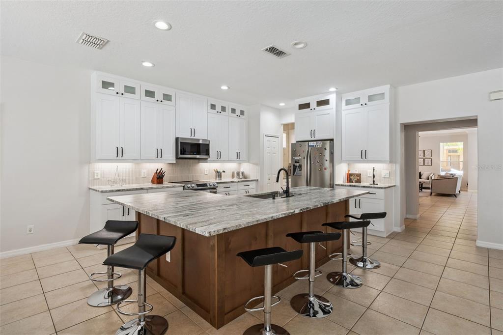 A kitchen features white upper cabinets, a wood-toned island with bar seating, and granite countertops — 110 ORANGE COSMOS BOULEVARD, DAVENPORT, FL