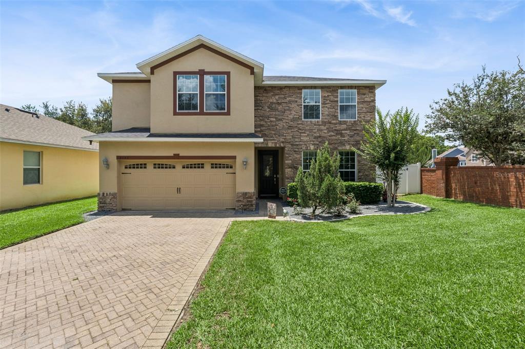 A two-story house with a stone facade, tan stucco, and a paved driveway — 2708 PEPPER LANE, ORLANDO, FL