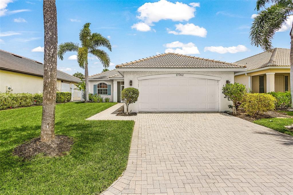 A single-story house with a white garage door, a paved driveway, and a palm tree — 17762 COURTSIDE LANDINGS CIRCLE, PUNTA GORDA, FL