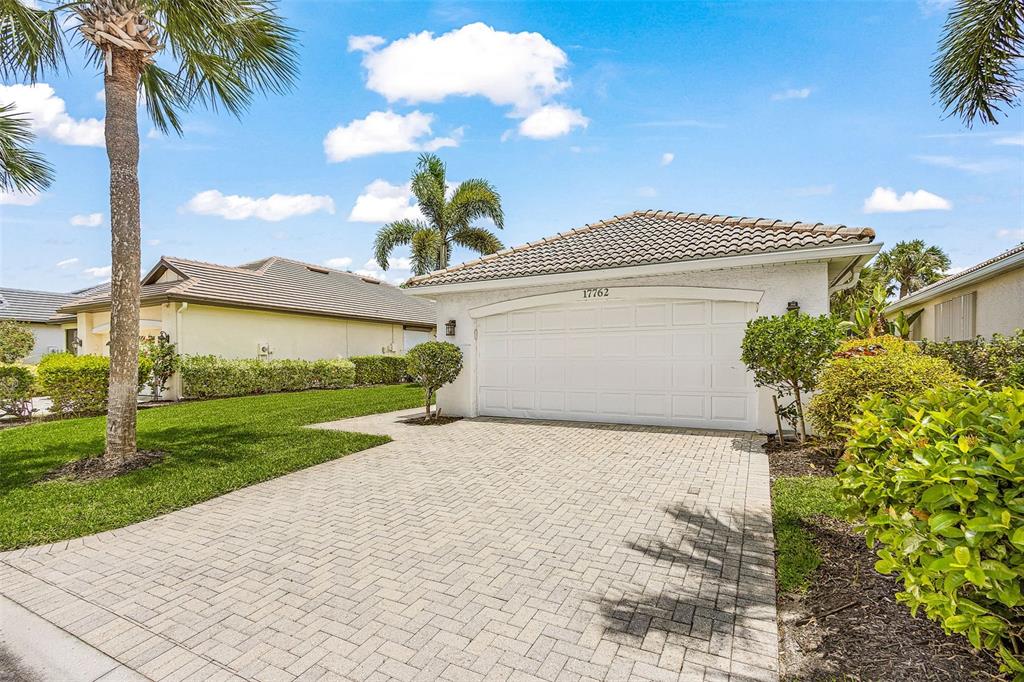 A single-story house with a white garage door and a paved driveway under a blue sky — 17762 COURTSIDE LANDINGS CIRCLE, PUNTA GORDA, FL