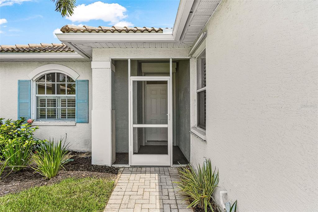 A paved walkway leads to a covered front entryway with a white screen door — 17762 COURTSIDE LANDINGS CIRCLE, PUNTA GORDA, FL