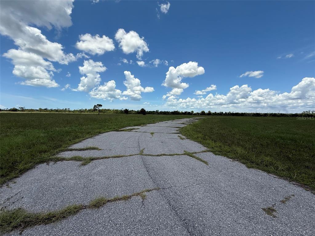 A cracked asphalt path winds through a large, grassy field under a blue sky — 12439 GREENLING WAY, PLACIDA, FL