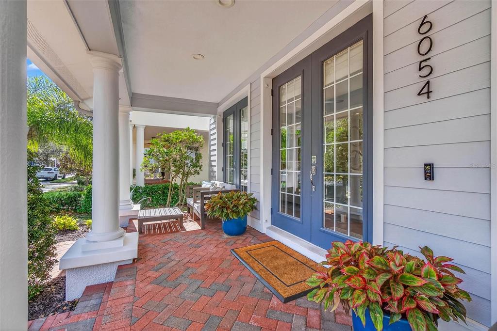 A covered front porch features brick pavers, blue double doors, and potted plants — 6054 YEATS MANOR DRIVE, TAMPA, FL
