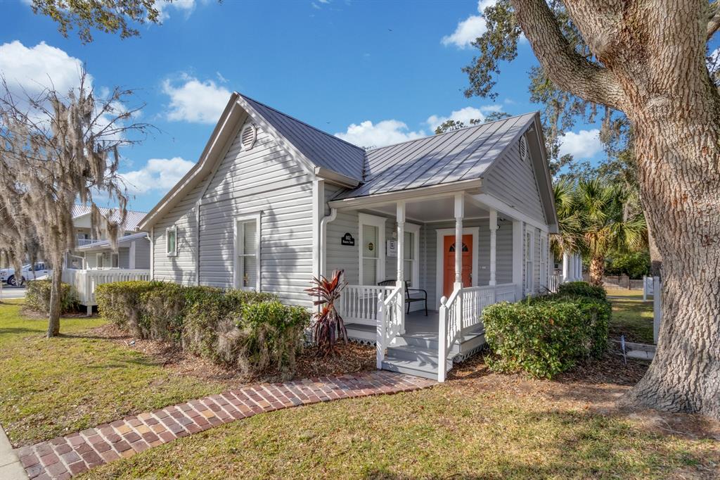 A light gray cottage with a metal roof, front porch, and brick walkway under trees — 802 MABBETTE ST, KISSIMMEE, FL