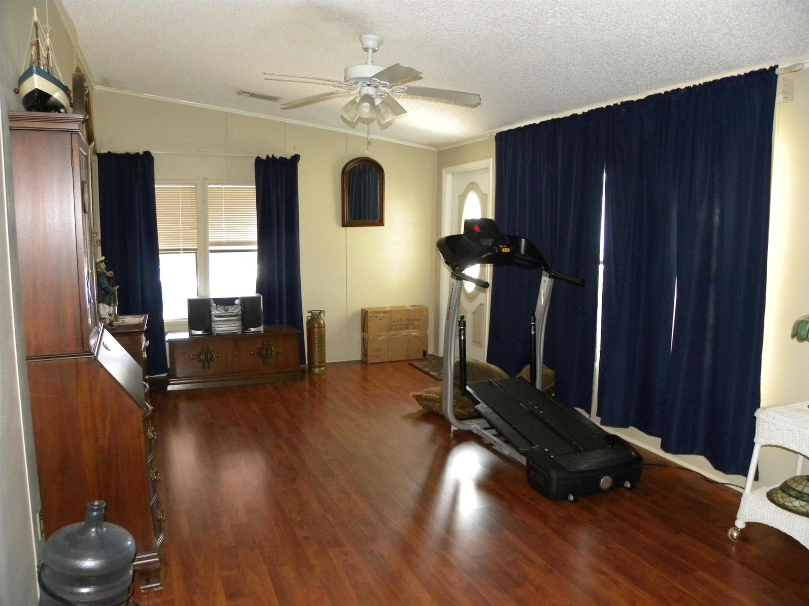 A room with wood-look flooring, a treadmill, dark blue curtains, and a ceiling fan — 456 Tropical Isles Circle, Fort Pierce FL 34982, FORT PIERCE, FL