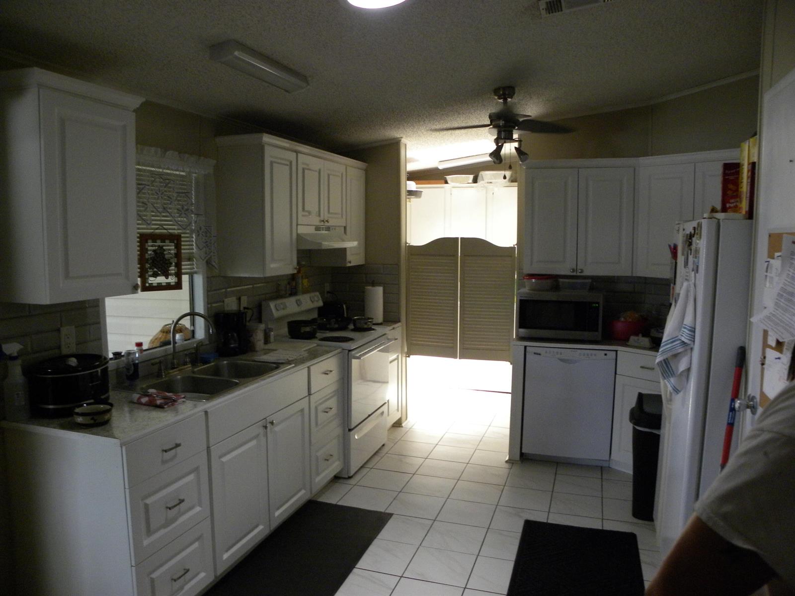 A kitchen with white cabinets, white appliances, tiled floors, and swinging doors leading to another room — 456 Tropical Isles Circle, Fort Pierce FL 34982, FORT PIERCE, FL