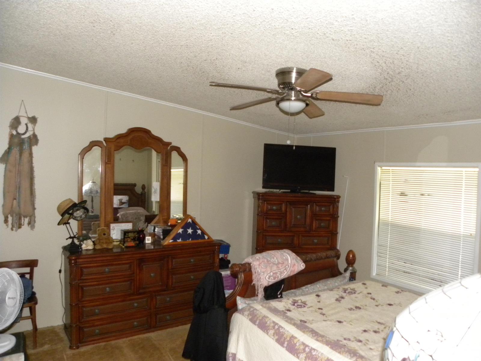 A bedroom features a wooden dresser with a mirror, a television, and a ceiling fan — 456 Tropical Isles Circle, Fort Pierce FL 34982, FORT PIERCE, FL