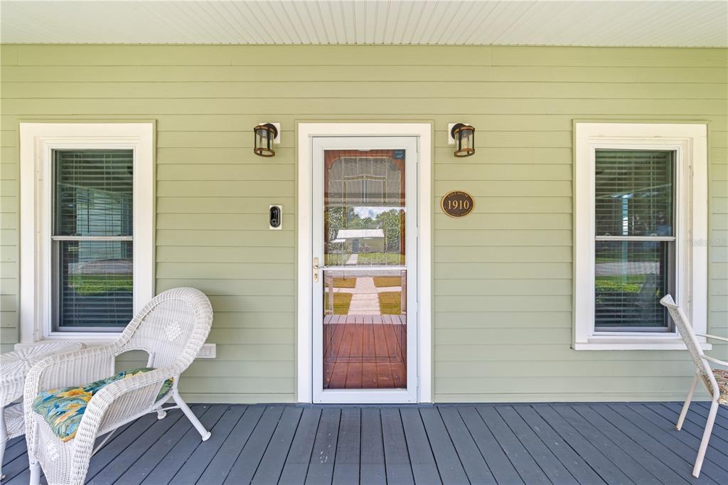 A covered porch with light green siding, a white storm door, and two wicker chairs — 714 MASSACHUSETTS AVENUE, ST CLOUD, FL
