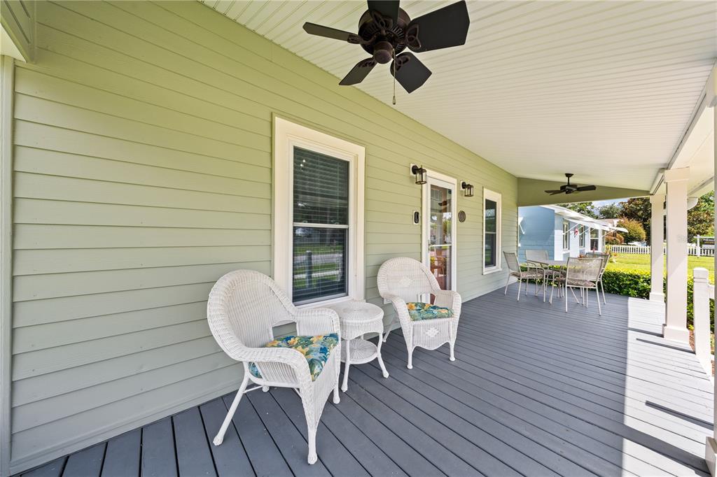 A covered porch with light green siding, gray decking, and white wicker patio furniture — 714 MASSACHUSETTS AVENUE, ST CLOUD, FL