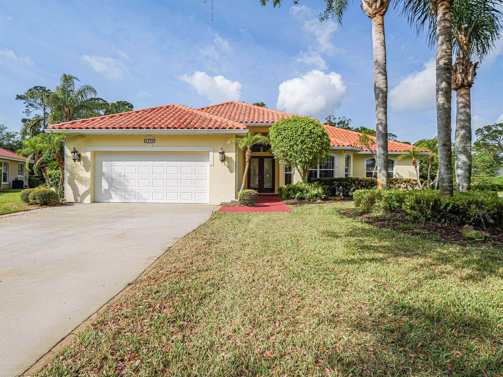 A single-story house with a red tile roof, beige stucco walls, and a two-car garage — 5873 Pine Ridge Circle, Vero Beach FL 32967, VERO BEACH, FL